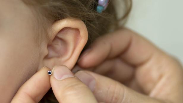 Einem Kind wird ein Ohrring eingesetzt.