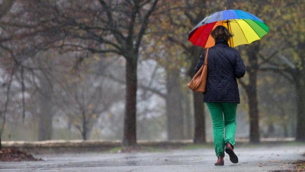 Eine Frau geht mit einem Regenbogen-Regenschirm im Regen spazieren.
