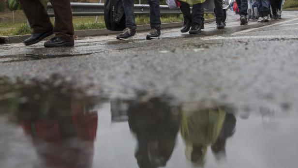 Eine Gruppe von Menschen geht auf einer nassen Straße, ihr Spiegelbild ist in einer Pfütze zu sehen.