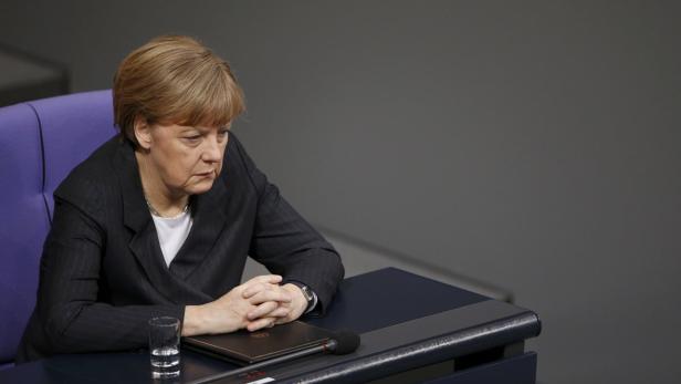 Angela Merkel sitzt mit verschränkten Händen an einem Tisch.