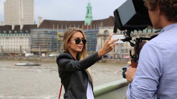Eine Frau macht ein Selfie vor der Londoner Skyline, während ein Kameramann sie filmt.