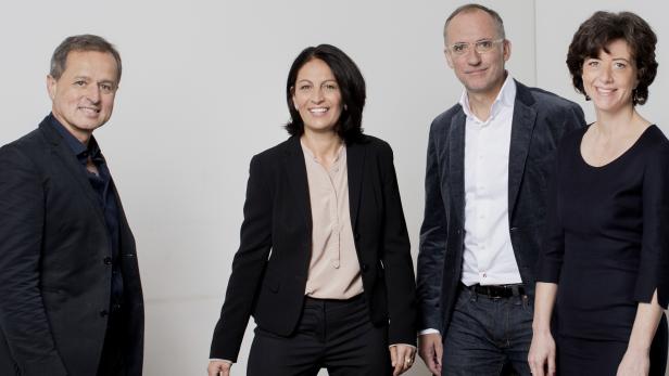 Eine Gruppe von vier Personen posiert vor einem hellen Hintergrund.