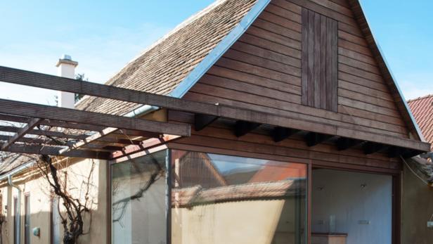 Ein modernes Haus mit Glasfront und Holzdach unter blauem Himmel.