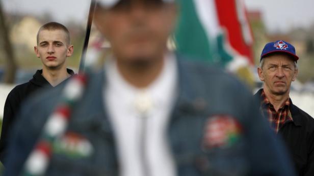 Drei Männer stehen vor einer ungarischen Flagge.