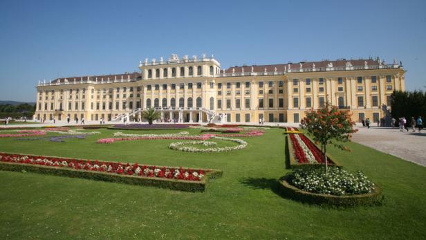 Schloss Schönbrunn in Wien mit kunstvoll angelegten Blumenbeeten im Vordergrund.
