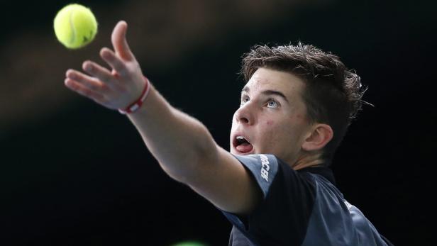 Ein Tennisspieler wirft einen gelben Tennisball in die Luft.