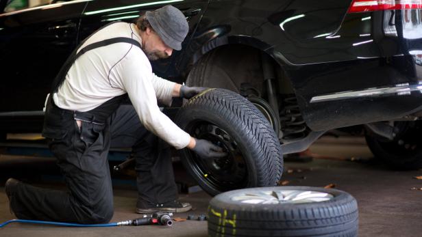 Ein Mechaniker wechselt einen Reifen an einem schwarzen Auto.