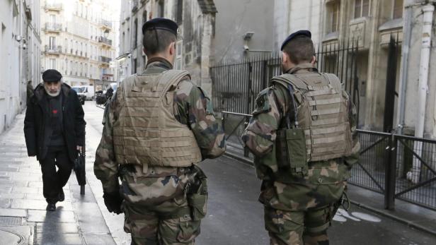 Zwei Soldaten patrouillieren vor einer Synagoge, während ein Mann vorbeigeht.