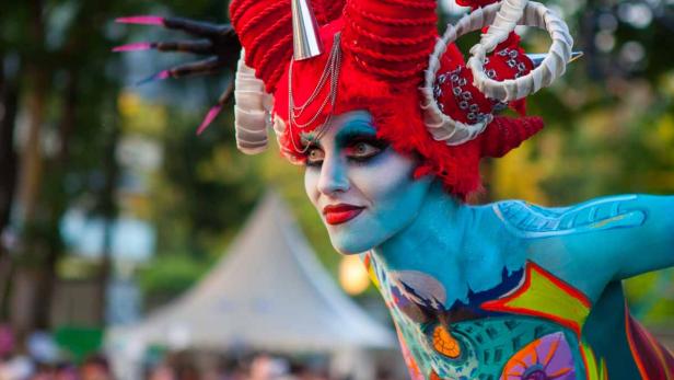 Eine Frau mit blauer Körperbemalung und einem roten, gehörnten Kopfschmuck.