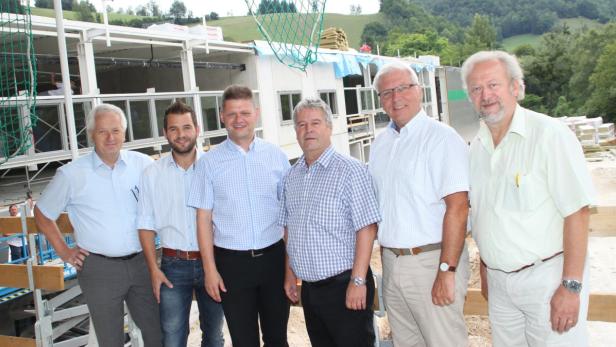 Eine Gruppe von sechs Männern posiert vor einem im Bau befindlichen Gebäude.