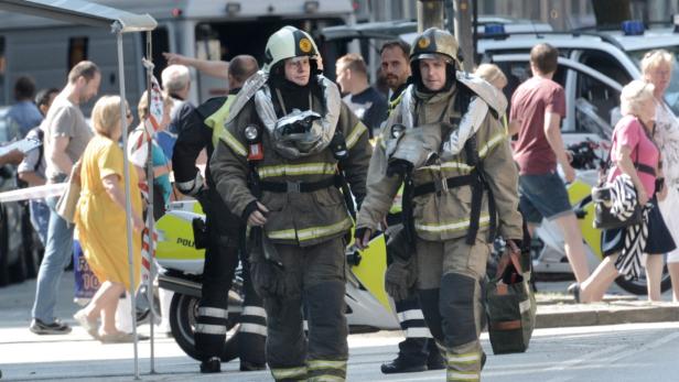 Zwei Feuerwehrleute in voller Montur gehen durch eine belebte Straße.