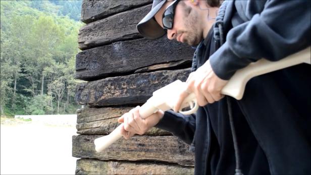 Ein Mann mit Sonnenbrille hantiert mit einer hellen, möglicherweise ungeladenen Waffe.