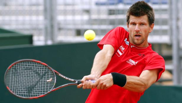 Ein Tennisspieler in rotem Trikot schlägt einen gelben Tennisball.