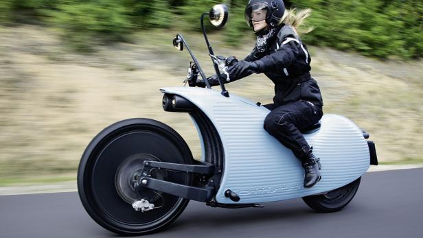 Eine Frau fährt ein hellblaues, futuristisch anmutendes Elektromotorrad.