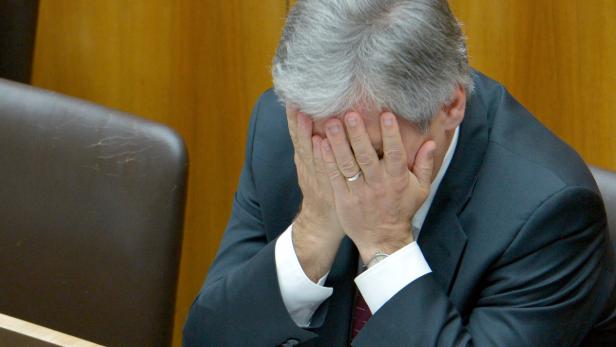 Ein Mann im Anzug sitzt mit verdecktem Gesicht da.