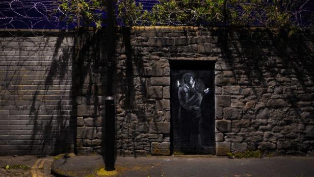 Ein Banksy-Graffiti zeigt ein sich umarmendes Paar, das auf ihre Handys schaut.