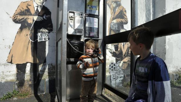 Ein Junge telefoniert in einer Telefonzelle, die mit Graffiti von Filmfiguren bemalt ist.