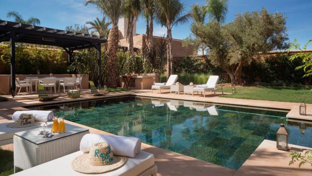 Ein Swimmingpool umgeben von Liegestühlen und tropischer Vegetation in einem Resort.