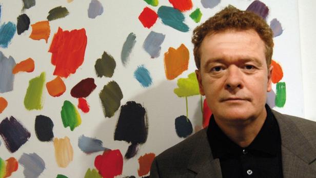 Ein Mann steht vor einem farbenfrohen abstrakten Gemälde.