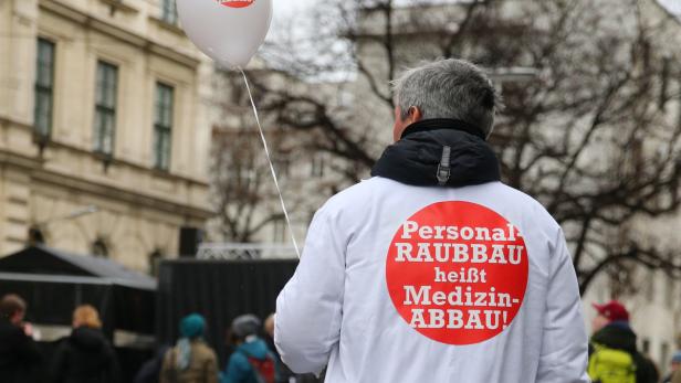 Eine Person in einem weißen Kittel mit der Aufschrift „Personal Raubbau heißt Medizin-Abbau!“ auf dem Rücken.