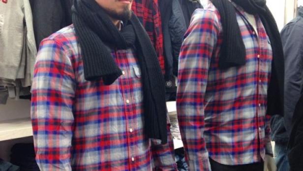 Ein Mann und eine Schaufensterpuppe tragen das gleiche karierte Hemd und einen schwarzen Schal.