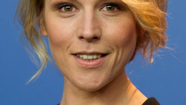 Porträt einer lächelnden Frau mit blonden Haaren vor blauem Hintergrund.