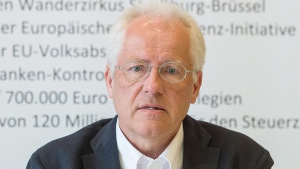 Ein Mann mit Brille steht vor einer Wand mit Text.