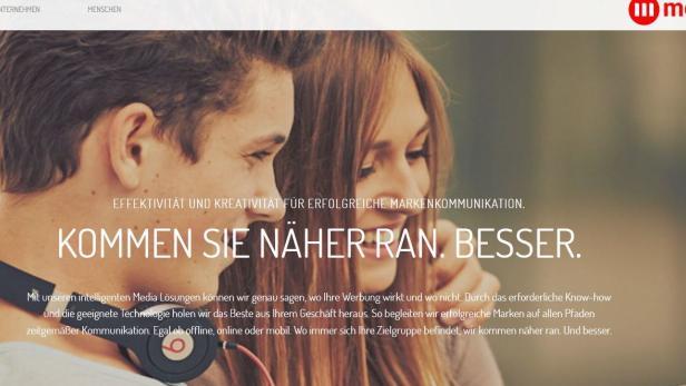 Ein Mann mit Kopfhörern und eine Frau sind auf einem Werbebildschirm von media.at zu sehen.