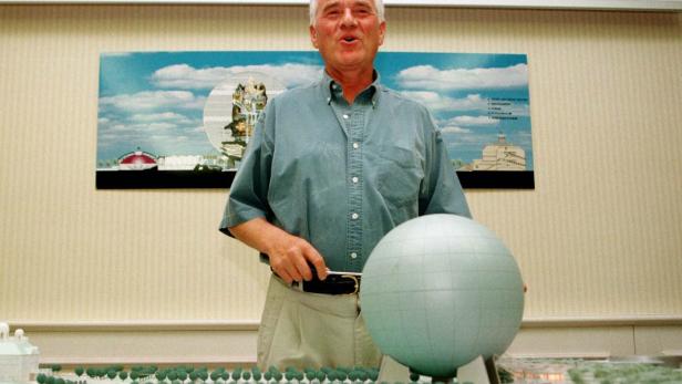 Ein Mann steht vor einem Modell eines Parks mit einem Globus in der Hand.