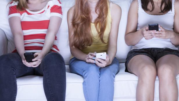 Drei junge Frauen sitzen auf einem Sofa und schauen auf ihre Smartphones.