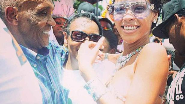Rihanna lächelt mit Fans und trägt eine auffällige Sonnenbrille und Schmuck.