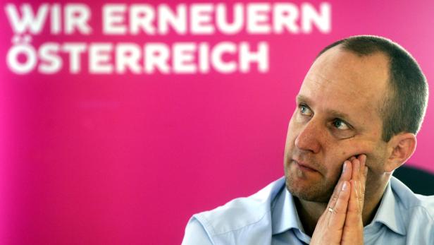 Ein Mann denkt vor einem pinkfarbenen Hintergrund mit der Aufschrift „Wir erneuern Österreich“ nach.
