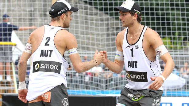 Zwei Beachvolleyballspieler aus Österreich geben sich die Hand am Netz.