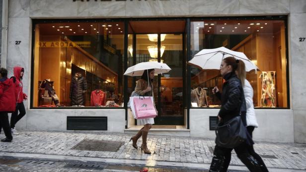 Frauen mit Regenschirmen gehen an einem Schaufenster vorbei.