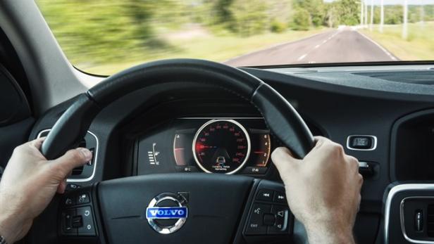 Die Hände eines Fahrers halten das Lenkrad eines Volvo auf einer Landstraße.