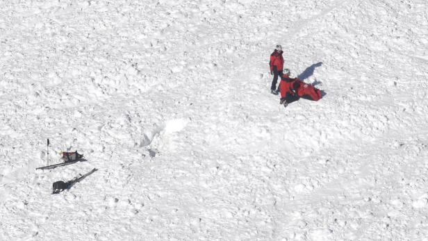 Zwei Rettungskräfte versorgen eine verletzte Person in einer roten Rettungstasche im Schnee.
