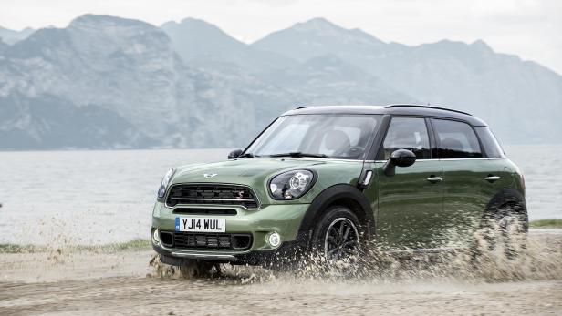 Ein grüner Mini Countryman fährt durch eine Wasserfläche vor einer Bergkulisse.