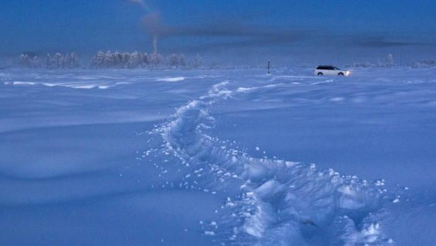 Eine Spur im Schnee führt zu einem Auto in einer verschneiten Landschaft unter einem Mondschein.