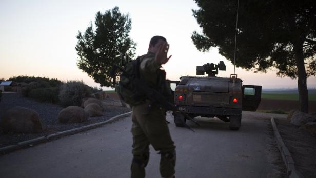 Ein Soldat steht mit erhobener Hand vor einem Militärfahrzeug.