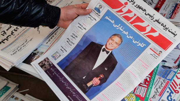 Eine Person hält eine iranische Zeitung mit einem Bild von George Clooney, der einen Golden Globe hält.