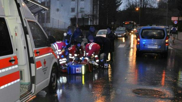 Rettungskräfte versorgen eine Person auf der nassen Straße neben einem Rettungswagen.