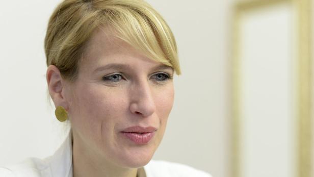 Eine Frau mit blonden Haaren und goldenen Ohrringen schaut zur Seite.