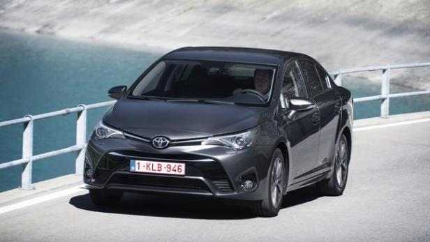 Ein grauer Toyota Avensis fährt auf einer Straße entlang eines Sees.