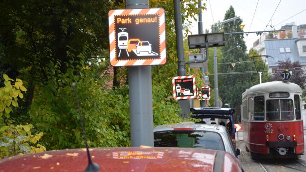 Ein Warnschild „Park genau!“ steht neben einer parkenden Straßenbahn.