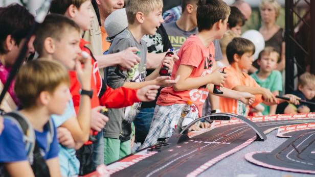 Eine Gruppe Kinder spielt mit einer Carrera-Rennbahn.