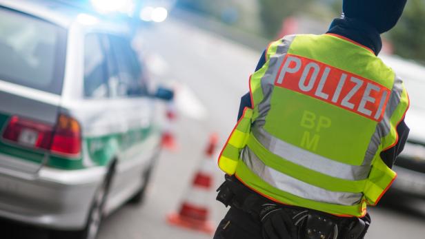 Ein Polizist steht neben einem Streifenwagen mit eingeschaltetem Blaulicht.