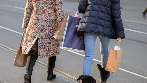 Zwei Frauen mit Einkaufstüten überqueren eine Straße.