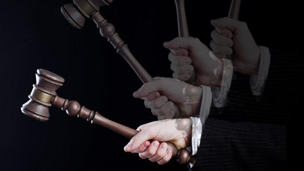 Eine Hand schwingt einen hölzernen Richterhammer vor einem schwarzen Hintergrund.