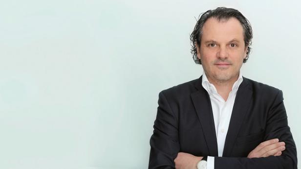 Ein Mann mit verschränkten Armen in einem dunklen Anzug und einem weißen Hemd.
