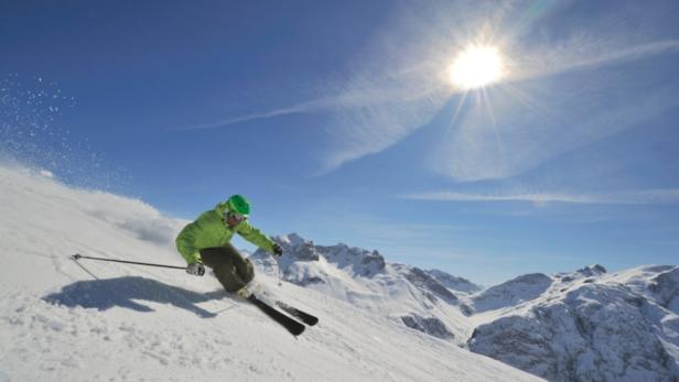 Ein Skifahrer fährt an einem sonnigen Tag eine schneebedeckte Piste hinunter.
